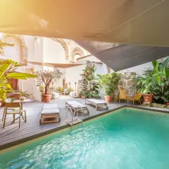Courtyard pool with lounge chairs, lush plants, and a decorative barrel under a sunshade.