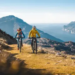 Coppia in mountain bike sui percorsi mtb Trentino, con vista mozzafiato sul lago e le montagne.