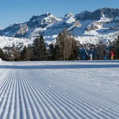 Piste da sci perfettamente battute a Pinzolo, con sciatori sullo sfondo e maestose montagne innevate.