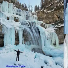 Un uomo in piedi sulla neve ammira le spettacolari cascate vallesinella ghiacciate, con stalattiti di ghiaccio che scendono dalle rocce.