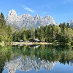 Riflessi perfetti sul lago Welsperg: montagne maestose, boschi verdi e un rifugio alpino.