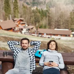 Un padre e un figlio si rilassano su una panchina in montagna, godendosi il sole dopo una passeggiata. Un perfetto weekend in montagna.