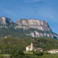 Imponente monte Macaion con vigneti terrazzati e un borgo con chiesa.