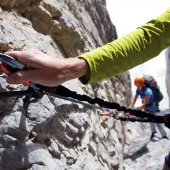 Mano agganciata a cavo d'acciaio su una parete rocciosa, un'avventura tra le ferrate Trentino con un'altra persona sullo sfondo.