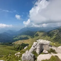 Rovine di un bunker sul **Castello Tesino**, con vista su verdi valli e montagne nebbiose sotto un cielo azzurro e nuvoloso.