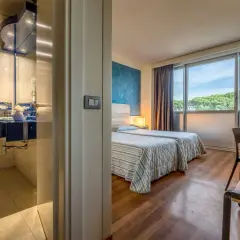 Camera d'albergo con due letti, bagno blu e vista sul verde. Ideale per sapere dove dormire a Pisa.