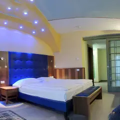 Camera moderna con letto king size e testiera blu imbottita, illuminazione soffusa e soffitto decorato. Un assaggio del comfort del Grand Hotel Astoria Lavarone.