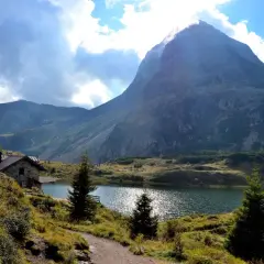 Sentiero che porta al **lago Colbricon**, con un rifugio in pietra e un maestoso monte sullo sfondo.