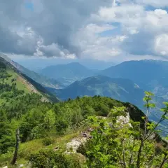Panoramica mozzafiato dal Monte Stivo, con valli verdi e montagne azzurre sotto un cielo nuvoloso.