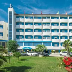 Hotel Olympic, un edificio bianco e blu con balconi, circondato da verde e fiori. Auto parcheggiate davanti.