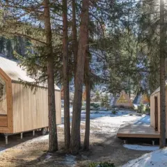 Piccole case in legno con grandi vetrate, immerse in un bosco innevato. Un'oasi di pace per alloggi particolari.