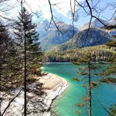 Un lago turchese incorniciato da alberi e montagne nel Val di Non. La spiaggia sabbiosa invita a una sosta.