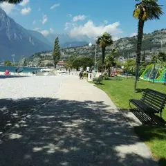 Vacanze in campeggio Europa a Torbole: spiaggia con windsurf, montagne sullo sfondo e area giochi per bambini.