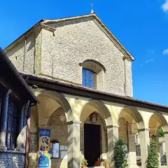 La Verna, luogo sacro con un portico ad archi che conduce all'ingresso di una chiesa in pietra, sotto un cielo azzurro.
