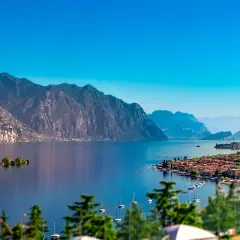 Un incantevole panorama per le tue vacanze sul Lago di Garda: montagne maestose, un'isola verde e un borgo pittoresco con barche a vela.