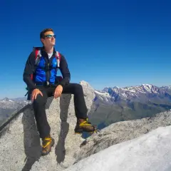 Giovane alpinista seduto sulla cima Presanella, ammira il panorama mozzafiato delle Alpi sotto un cielo azzurro.