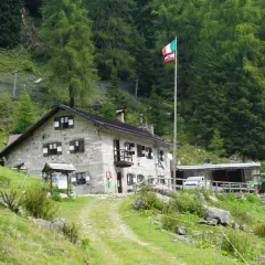 Il rifugio Trivena, con bandiera italiana, è una casa in pietra immersa nel verde, con un trattore parcheggiato accanto.