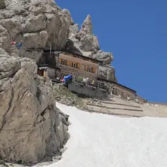 Rifugio Passo Principe, un rifugio alpino in legno incastonato tra rocce imponenti e neve, con un cielo azzurro limpido.