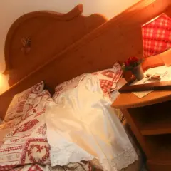 Camera accogliente all'hotel La Romantica Moena, con letto decorato e comodino con fiori.