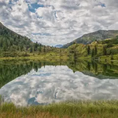 Lago alpino con riflessi di montagne e cielo nuvoloso, un'oasi di pace in una splendida cavalese estate.