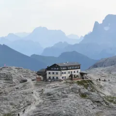 Il rifugio Rosetta, un edificio imponente, si erge su un terreno roccioso con montagne sfumate all'orizzonte.