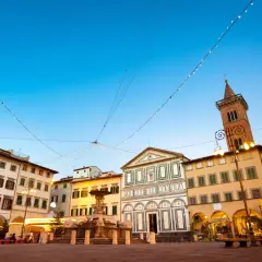 Piazza di Empoli illuminata da luci natalizie, con la fontana, la chiesa e il campanile che si stagliano sotto un cielo azzurro.