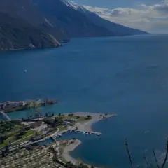 Vista panoramica del lago con montagne sullo sfondo. In primo piano, un lido e un camping vicino ad Arco.