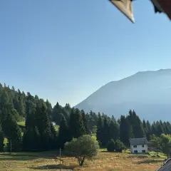 Un casolare bianco, forse la locanda La Ruscoletta, immerso nel verde di un prato e circondato da alberi, con montagne nebbiose sullo sfondo.