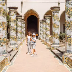 Un madre e figlio passeggiano tra colonne decorate con maioliche, un luogo incantevole tra i tanti posti da visitare a Napoli.