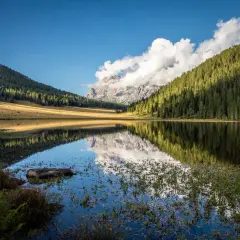 Riflessi perfetti sul lago di Calaita, con montagne imponenti e foreste verdi che si specchiano nell'acqua calma.