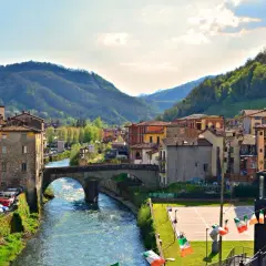 Borgo pittoresco in Garfagnana, cosa vedere: un fiume serpeggia tra case colorate e colline verdi, con un antico ponte in pietra.