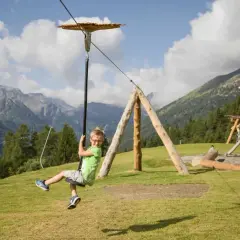 Bambino felice sfreccia su una teleferica nel **Pejo Kinderland**, con montagne sullo sfondo.