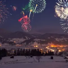 Fuochi d'artificio colorati illuminano il cielo notturno sopra un villaggio innevato, celebrando il capodanno in montagna.