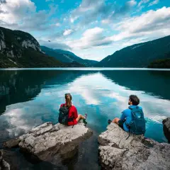 Coppia ammira il **lago di Molveno** da rocce, circondati da montagne verdi e cielo azzurro con nuvole bianche.
