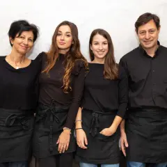 Four people, two women and two men, wearing black shirts and aprons, stand together smiling.