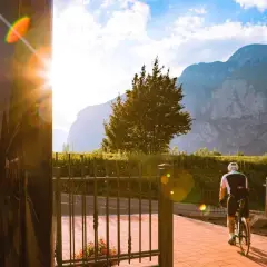 Ciclista in sella alla bici, con montagne sullo sfondo. Un raggio di sole illumina la scena vicino al bicigrill Faedo.