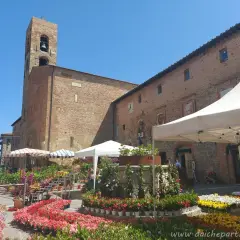 Mercato fiorito a Casole d'Elsa, con bancarelle colorate e un'antica torre campanaria sullo sfondo.