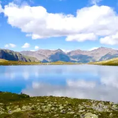 Un sereno lago alpino riflette il cielo azzurro e le montagne. Un paesaggio da sogno nel Trentino.