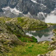 Due escursionisti ammirano un lago alpino e montagne imponenti, seguendo il sentiero della pace.