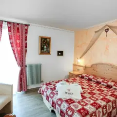 Camera accogliente con letto a quadri rossi, tende a cuoricini e un sacchetto con logo POSTA HOTEL 1899.