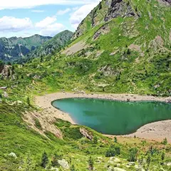Un rifugio solitario vicino al **lago di Erdemolo**, circondato da verdi pendii montuosi e un cielo azzurro con nuvole bianche.