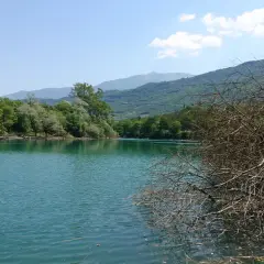 Acque turchesi del lago di Cavedine circondato da rigogliosa vegetazione e montagne sullo sfondo.