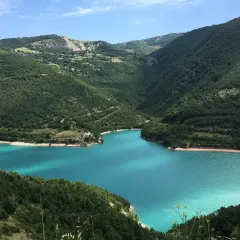 Splendido lago di Fiastra con acque turchesi, incastonato tra verdi colline boscose sotto un cielo azzurro.