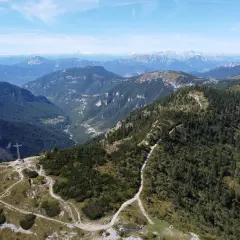 Sentiero che sale verso la croce sul monte Maggio, con vista su valli verdi e montagne all'orizzonte.