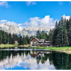 Riflessi sull'acqua del lago Nambino, con un rifugio alpino e montagne sullo sfondo.