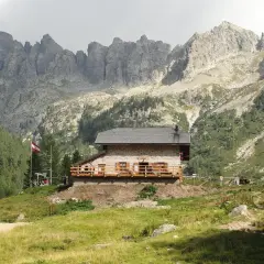 Il rifugio Caldenave, un'accogliente baita in pietra, si erge su un prato verde ai piedi di imponenti montagne rocciose.