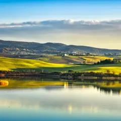 Dolci colline toscane illuminate dal sole al tramonto si specchiano nel lago di Santa Luce, creando un paesaggio incantevole.