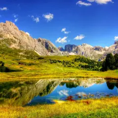 Un lago alpino riflette montagne maestose e prati verdi. Perfetto per le cose da fare in estate: escursioni, relax e ammirare la natura.