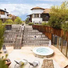 Relaxing at Pineta Nature Resort: un uomo prende il sole su una scalinata in legno, vicino a una vasca idromassaggio e a un edificio moderno.