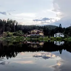 Riflessi serali sul lago di Santa Colomba, con un albergo e una casa immersi nel verde degli alberi.